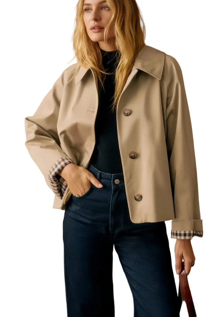 Woman wearing a beige jacket and dark jeans against a white background