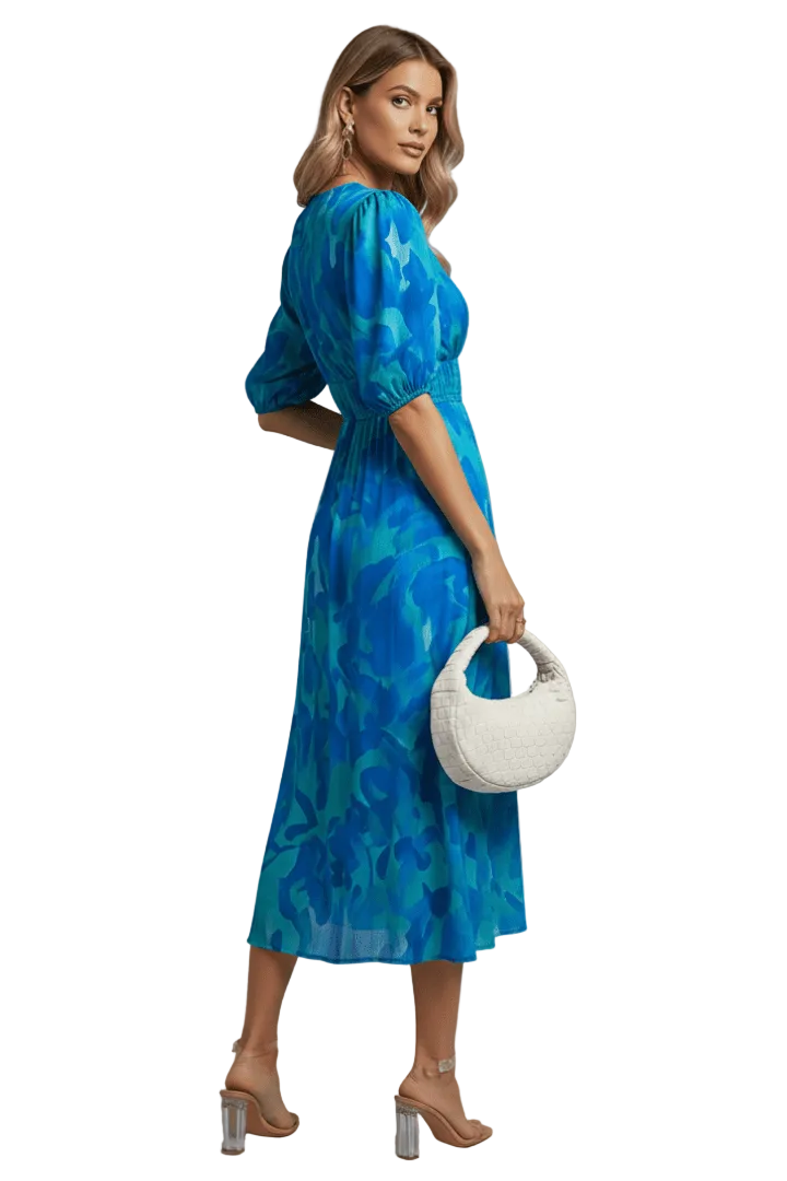 Woman wearing a blue floral dress holding a white handbag against a white background