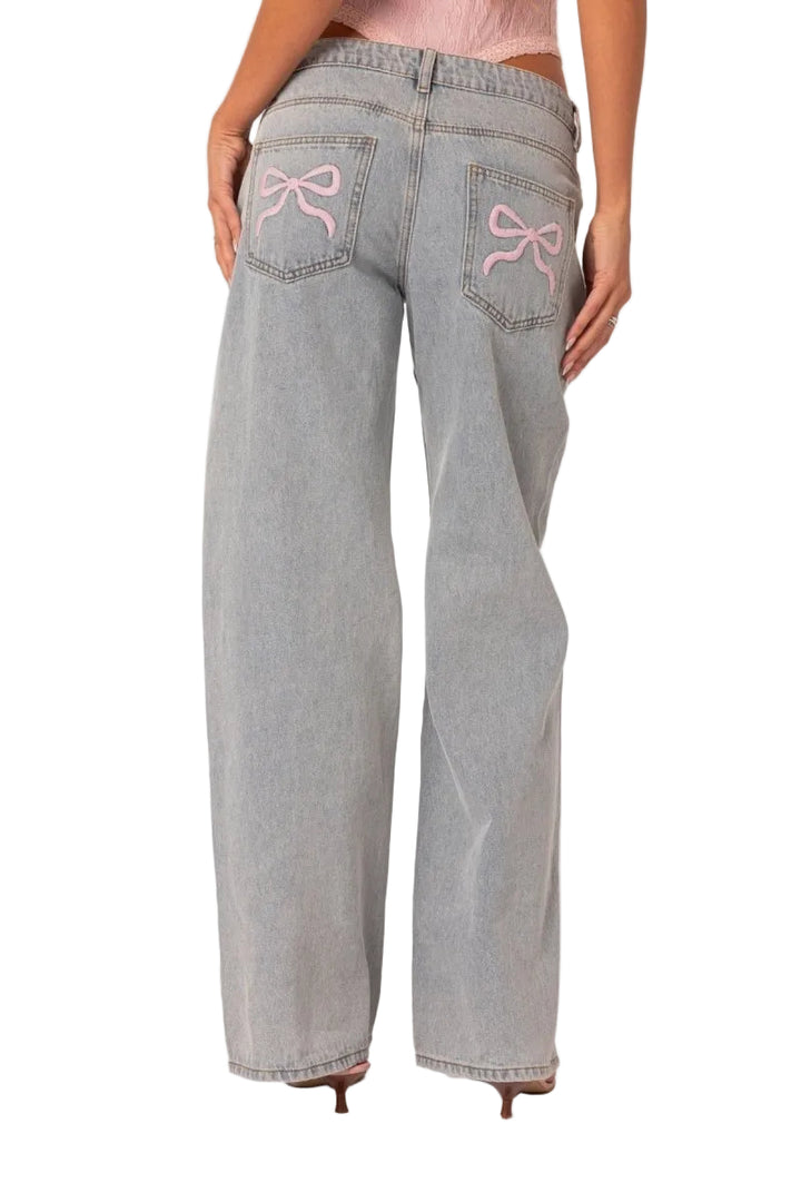 Light blue jeans with pink bow designs on the pockets against a white background