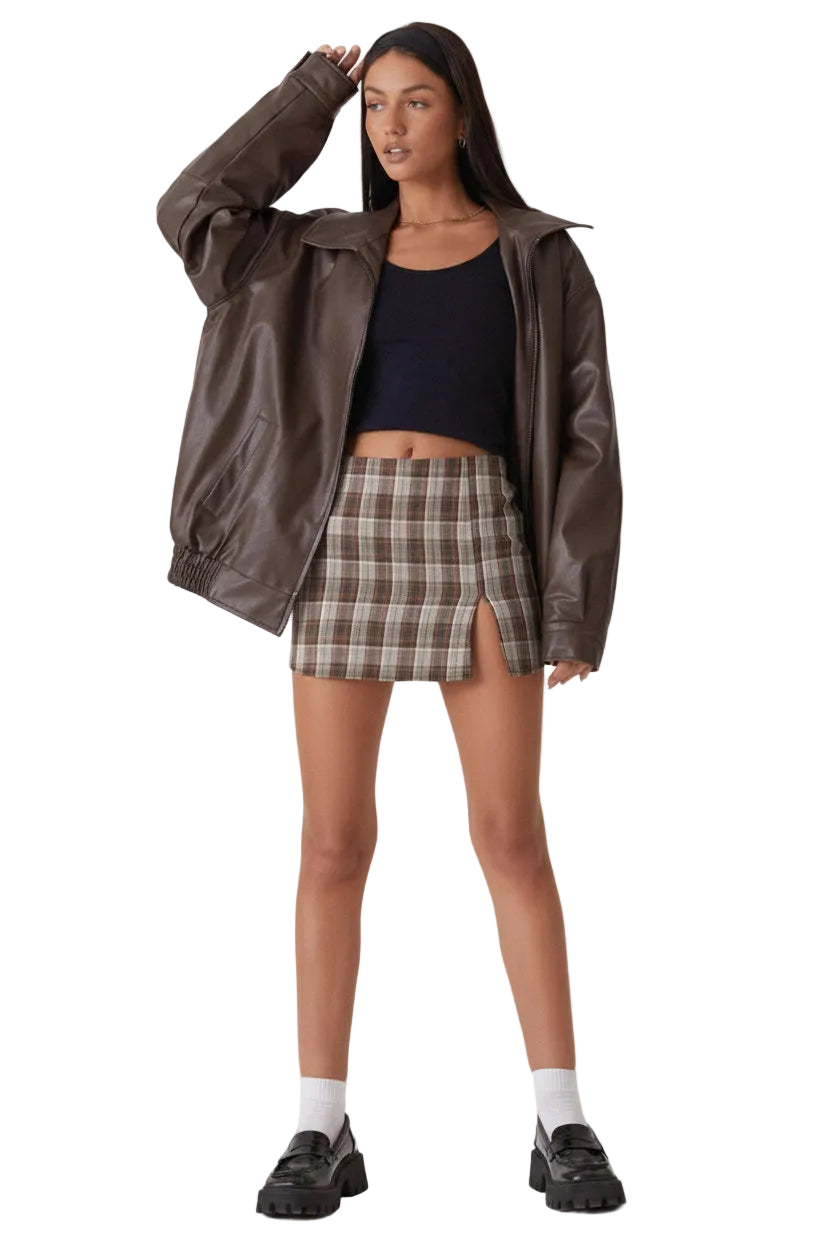 Woman wearing a brown jacket, black top, plaid skirt, and white socks on a white background