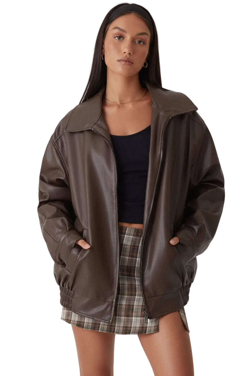 Woman wearing a brown leather jacket over a black top and plaid skirt on a white background