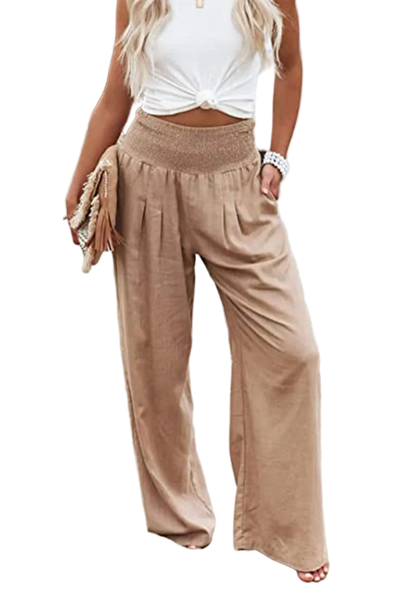 Woman wearing beige wide-leg pants and a white top by a body of water.