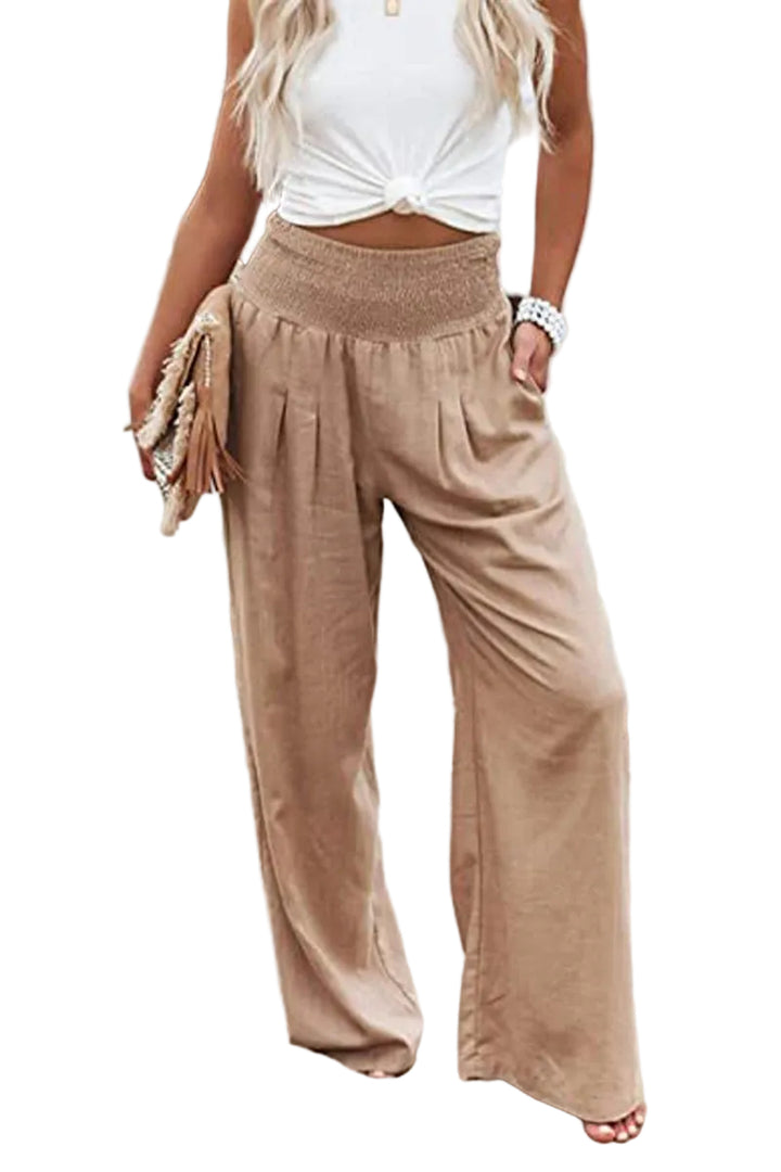 Woman wearing beige wide-leg pants and a white top by a body of water.