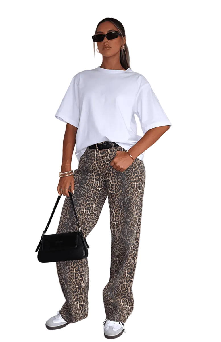 Person wearing a white t-shirt and leopard print pants with sunglasses and a black handbag indoors.
