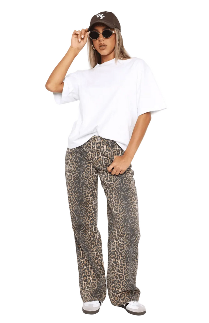 Person wearing a white oversized shirt, leopard print pants, and a cap on a white background